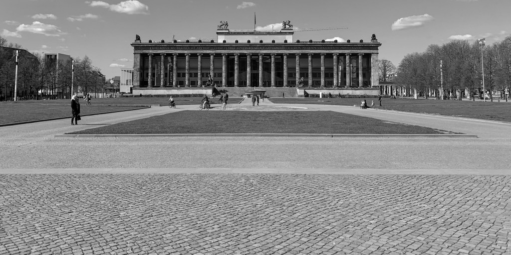 Almost empty Berlin square in front of a classical museum building, with a few distant figures.
