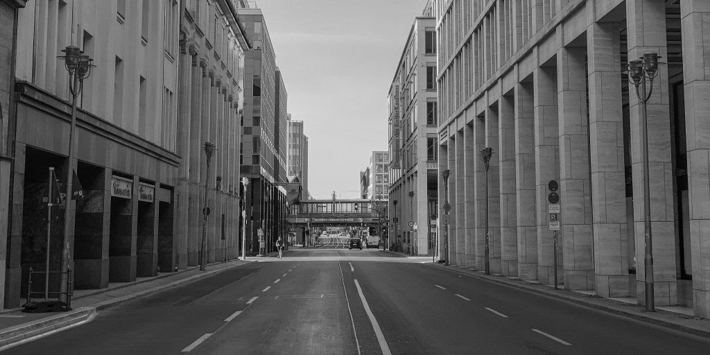 Empty Berlin street lined with modern buildings and a bridge in the distance.
