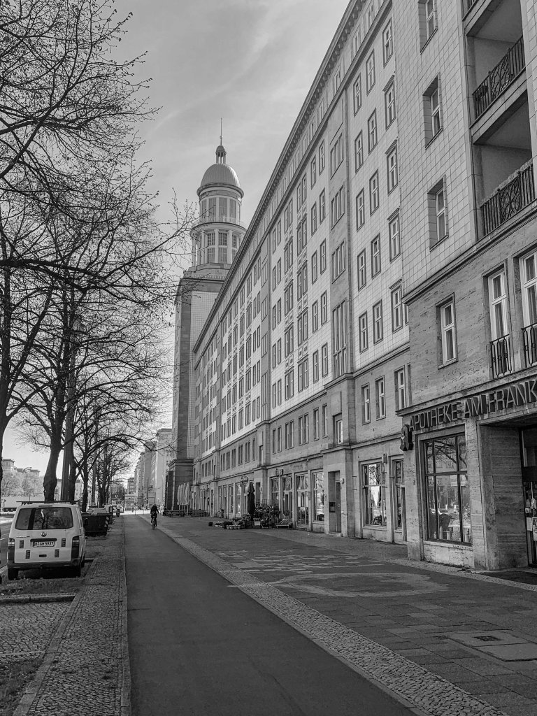 Wide Berlin street with the dome of the Französischer Dom and mostly empty pavements.