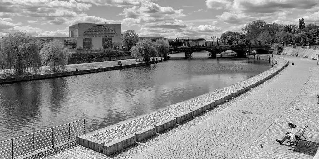 Empty riverside scene in Berlin with benches, bridge, museum building, and broad paved spaces.