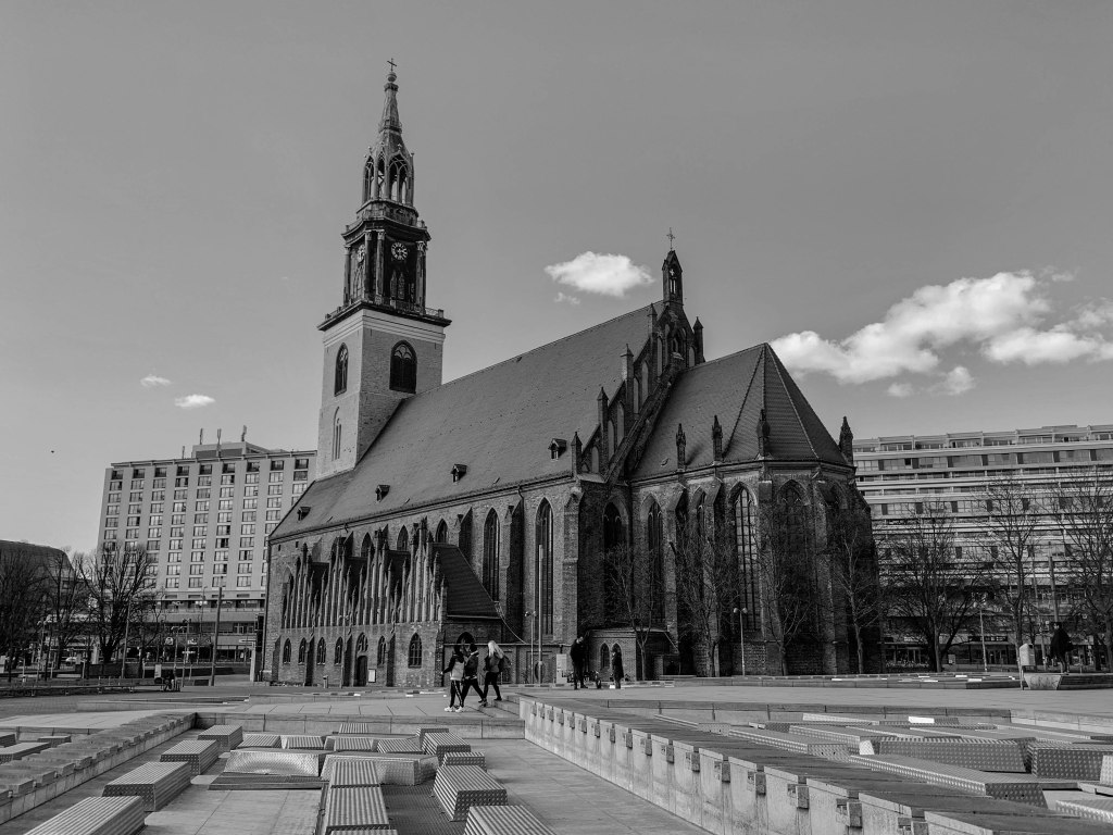 Berlin church and surrounding square with few pedestrians and geometric paving.