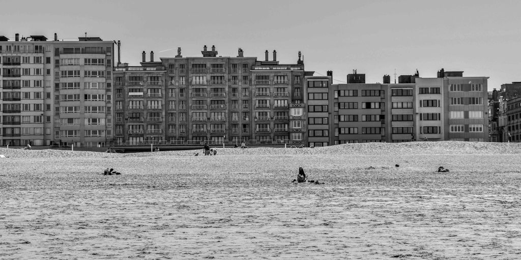 Ostende beach with sea in the foreground, small figures in the water, and a row of seafront apartment buildings.