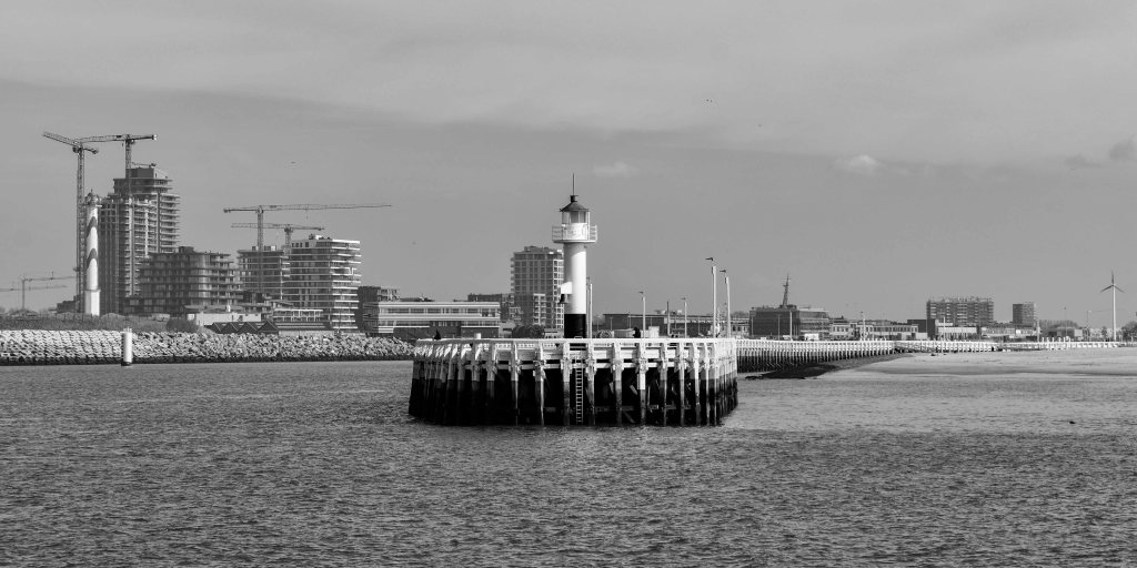 Ostende pier and small lighthouse with construction cranes and buildings in the background.