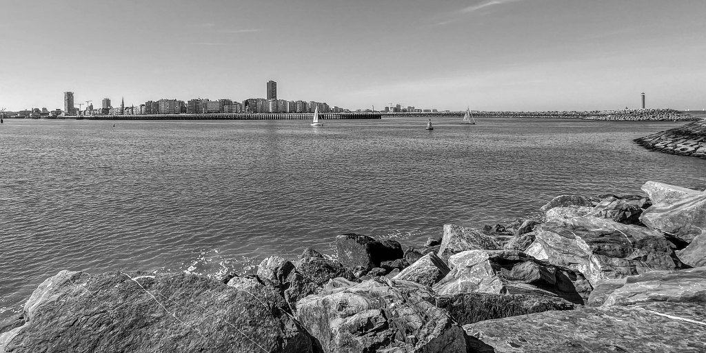 Wide view across water and rocks towards the Ostende skyline and harbour entrance.