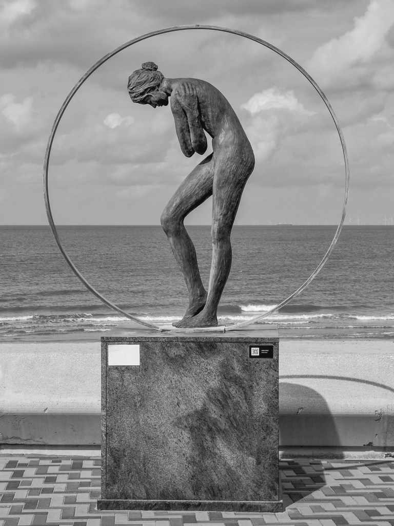 Seafront sculpture of a bent figure inside a circular frame, with the sea behind it.