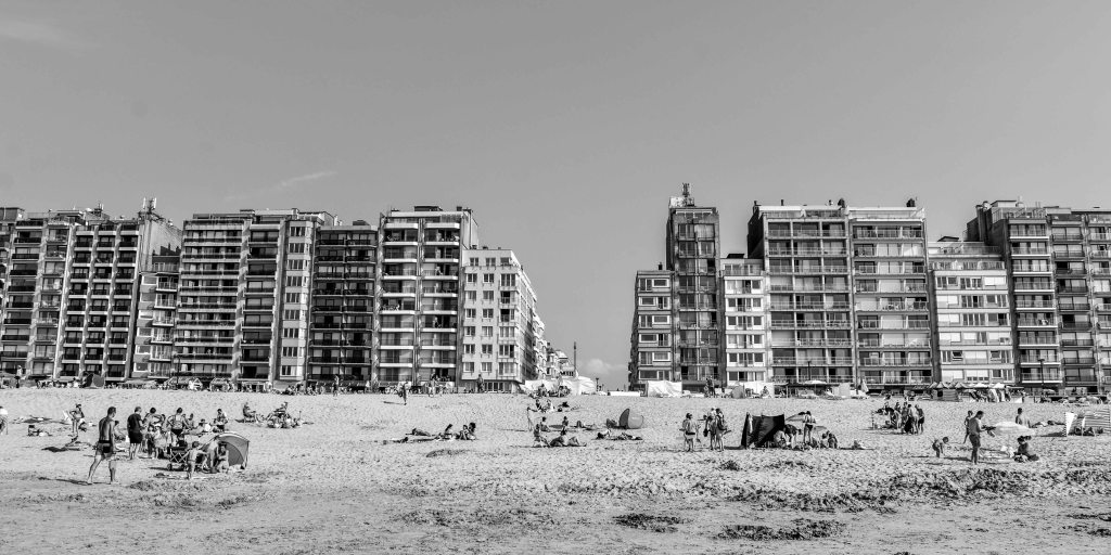 Belgian beach with rows of seafront apartment blocks and scattered groups of people on the sand.