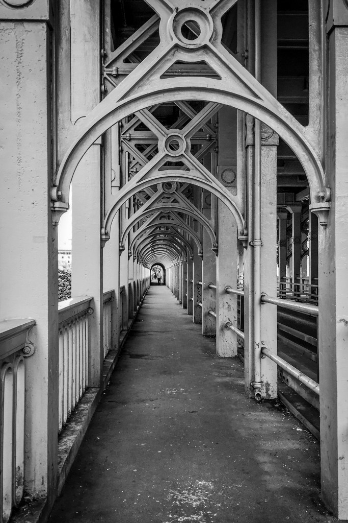 Long covered walkway with repeated metal arches, railings, and a vanishing point.