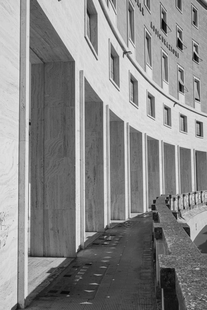 Curving modern colonnade with repeated rectangular openings, stone surfaces, and strong shadows.