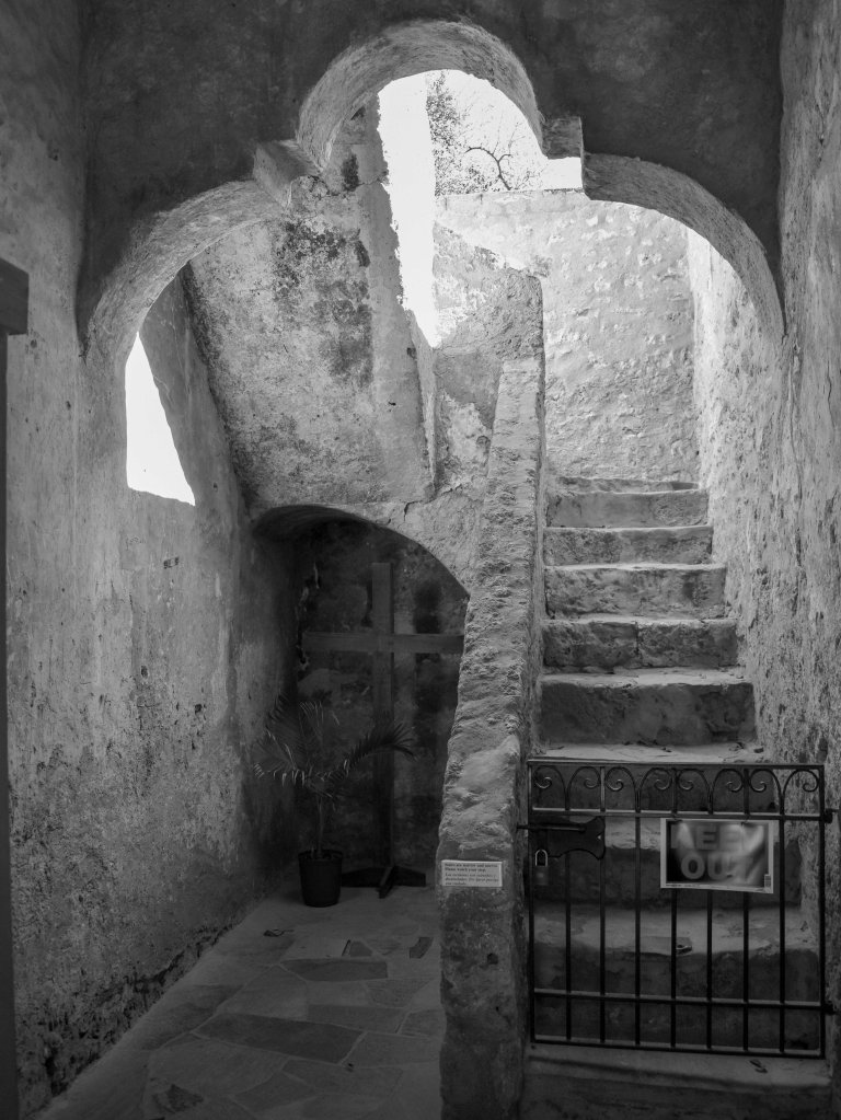 Rough stone interior passage with arched openings, stairway, and light entering from above.