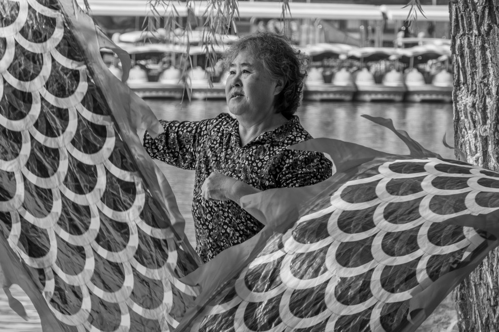 Woman playing with a large fabric dragon-shaped kite in Beijing.