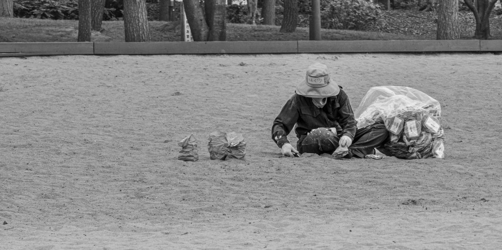 Person lying on sand beside bags in an open beach in Tokyo.