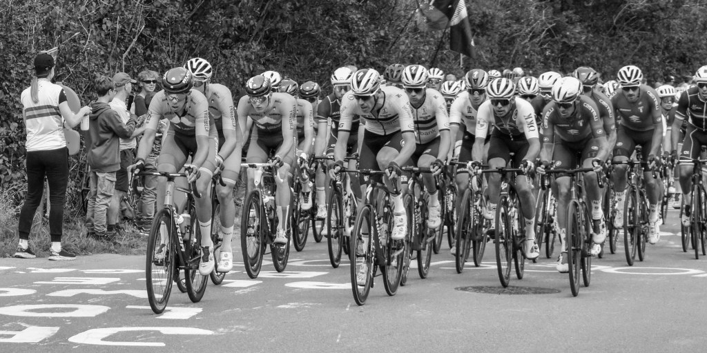 Close view of cyclists in the peloton, with helmets, team kits, bikes, and concentrated faces.