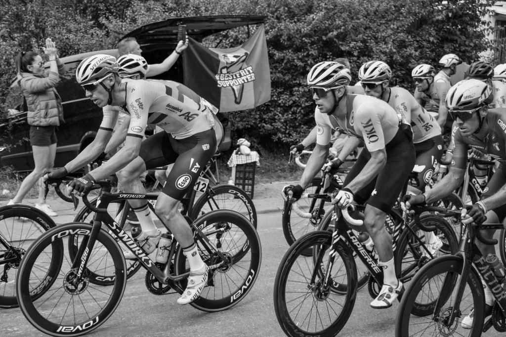 Group of cyclists riding closely together, with several riders leaning forward in effort.