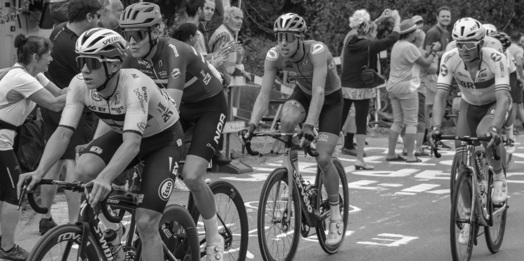 Group of cyclists riding closely together, with several riders leaning forward in effort.