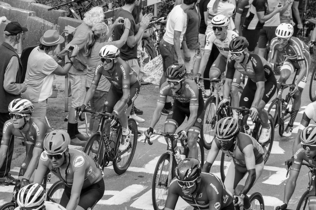 Dense cluster of cyclists riding through the crowd, with wheels, helmets, and bodies overlapping.