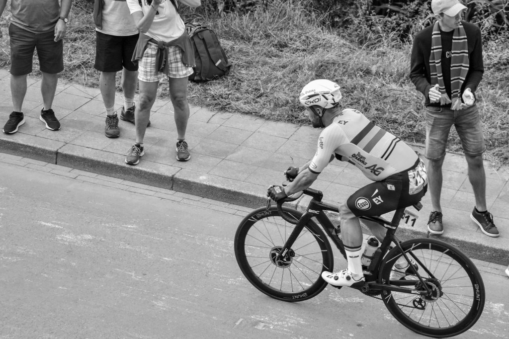 Lone cyclist riding past spectators on a wide stretch of road.