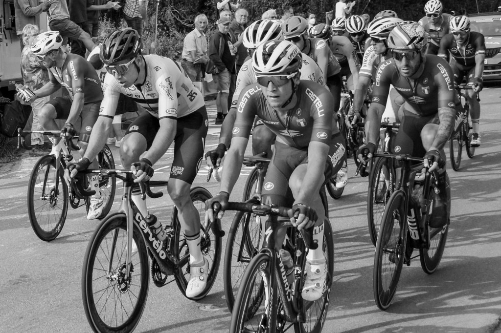 Group of cyclists riding together, with bodies low over the handlebars and faces marked by effort.