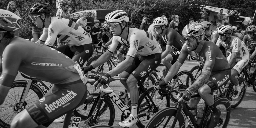 Tight side view of cyclists in the peloton, with wheels and team kits overlapping in motion.