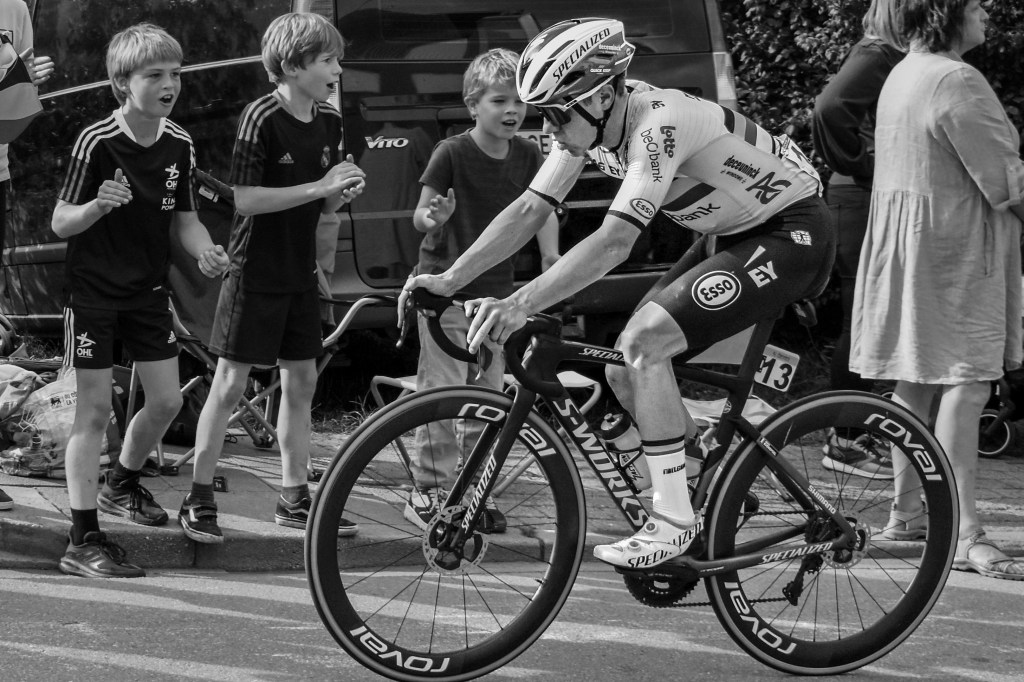 Close side view of a cyclist passing cheering children along the roadside.