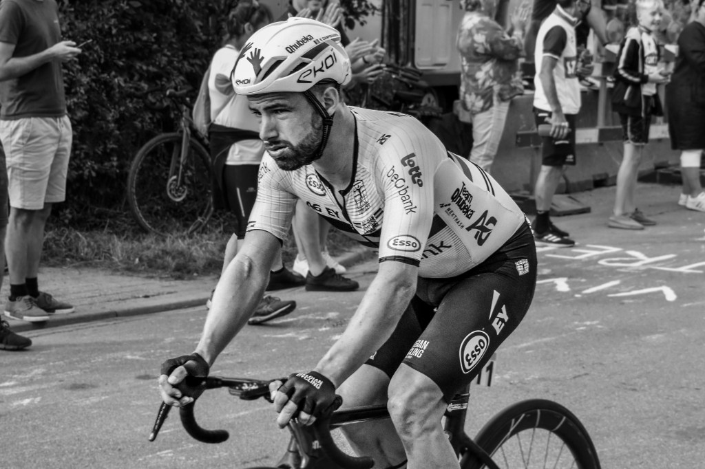 Close portrait of a cyclist in race kit and helmet, riding with a strained expression.