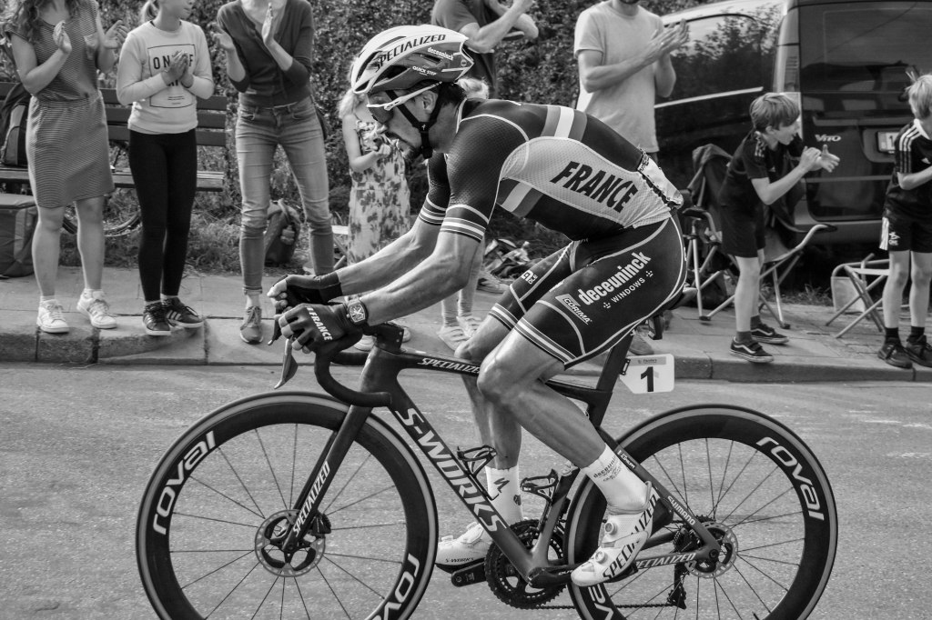 Alaphilippe riding in profile, bent low over the bike, with spectators in the background.
