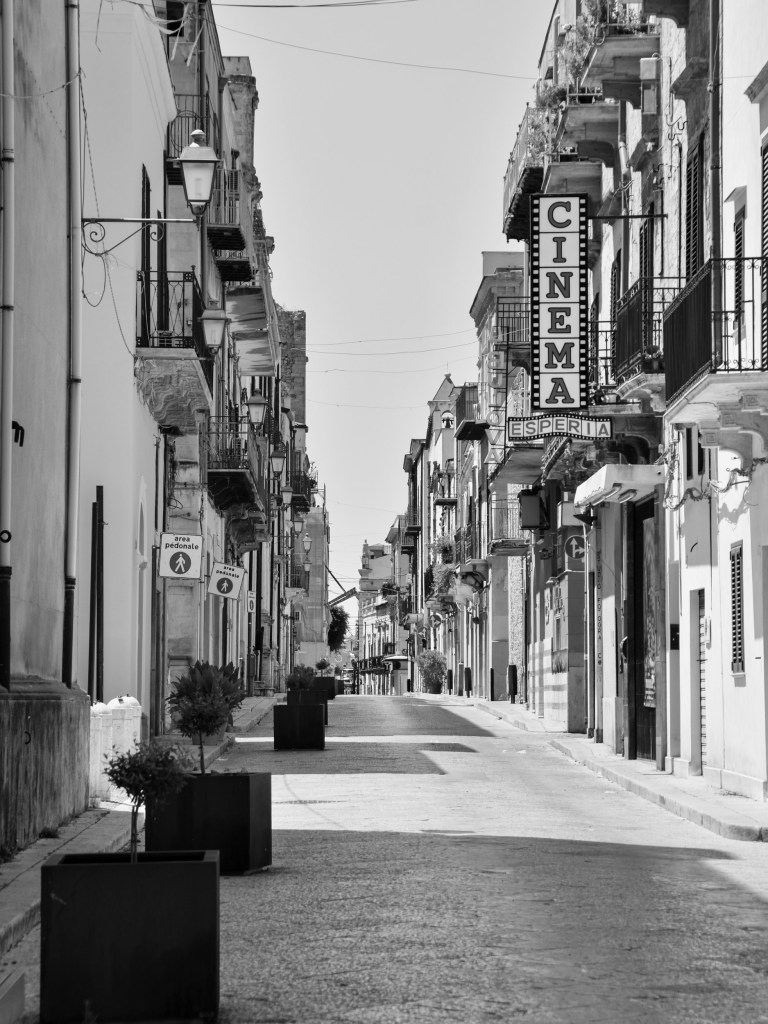 An empty central street is lined with balconies and lamps beneath the vertical Cinema Esperia sign.