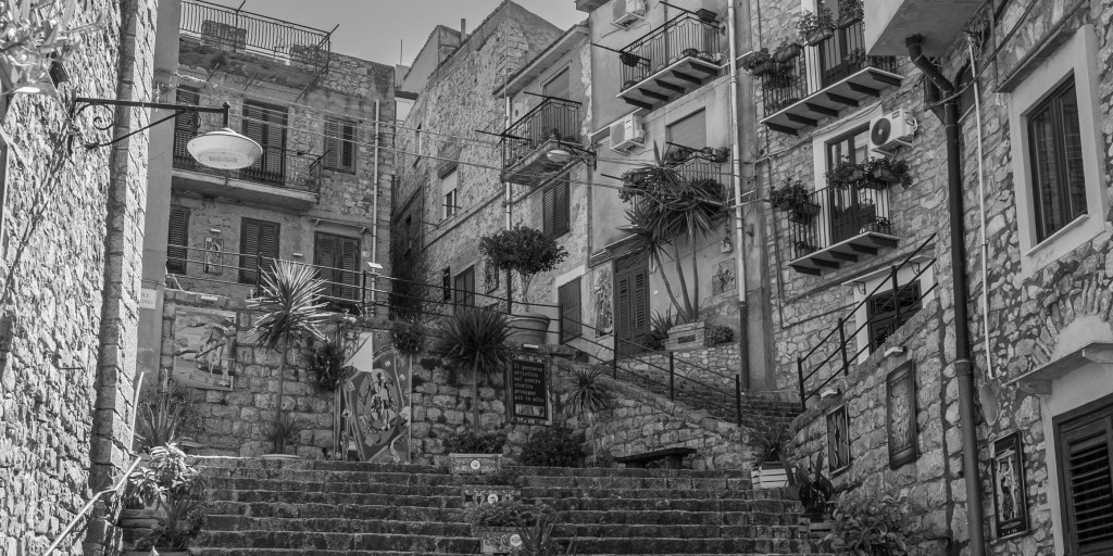 A broad stone staircase climbs between tightly packed houses with balconies, cables, signs and potted plants.