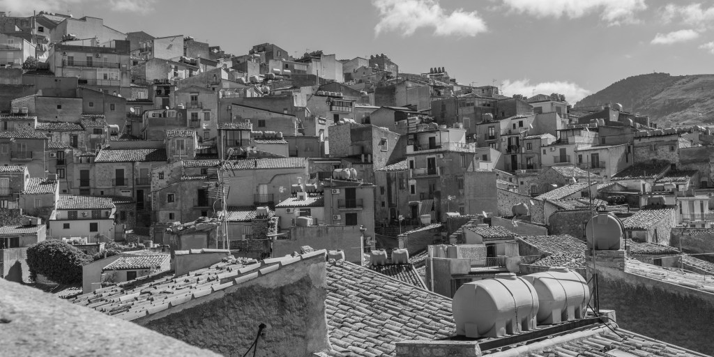 Dense houses and tiled roofs cover a hillside, punctuated by rooftop water tanks, balconies and television antennas.