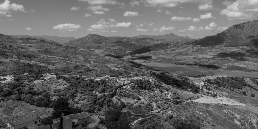 Rolling hills surround a long body of water beneath a wide sky scattered with small clouds.