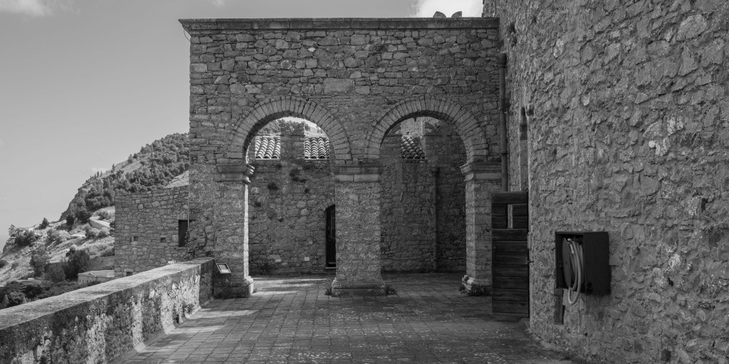 A stone terrace inside the castle ends at two broad arches, with a wooded hillside visible beyond.