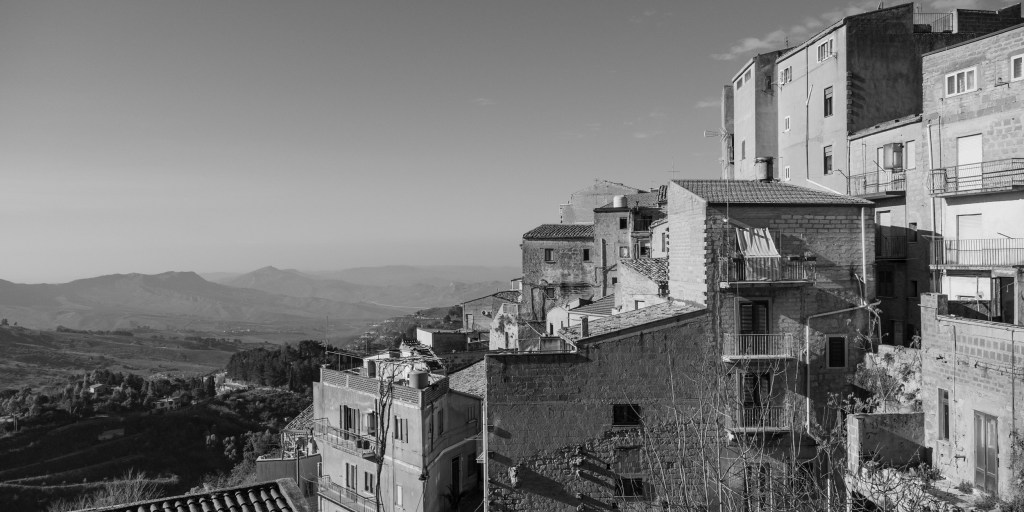 Houses cling to the edge of Calascibetta above a broad landscape of hills and valleys.