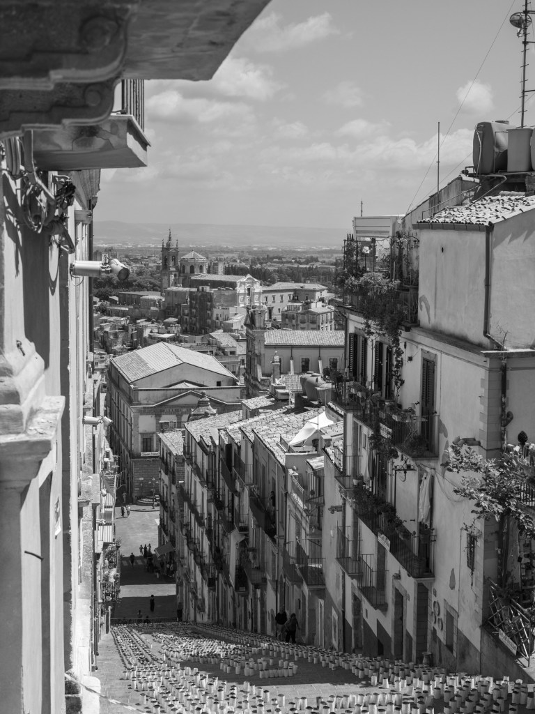 An elevated view looks down the decorated staircase and across Caltagirone’s rooftops, churches and surrounding plain.