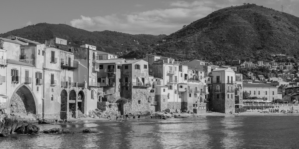 Historic waterfront buildings line the shore beneath the hills surrounding Cefalù.