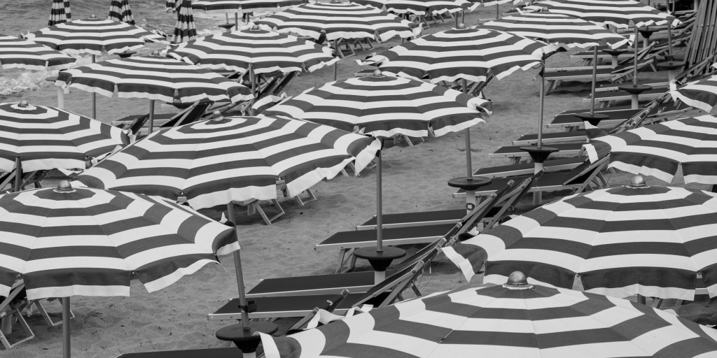 A dense pattern of striped umbrellas and empty sun loungers covers the beach.