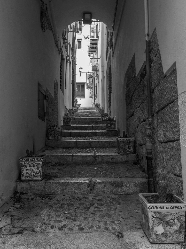 Stone steps climb beneath an archway between walls lined with decorated plant containers.