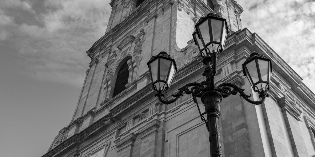 Three ornate streetlamps rise before the tall stone façade of a church.
