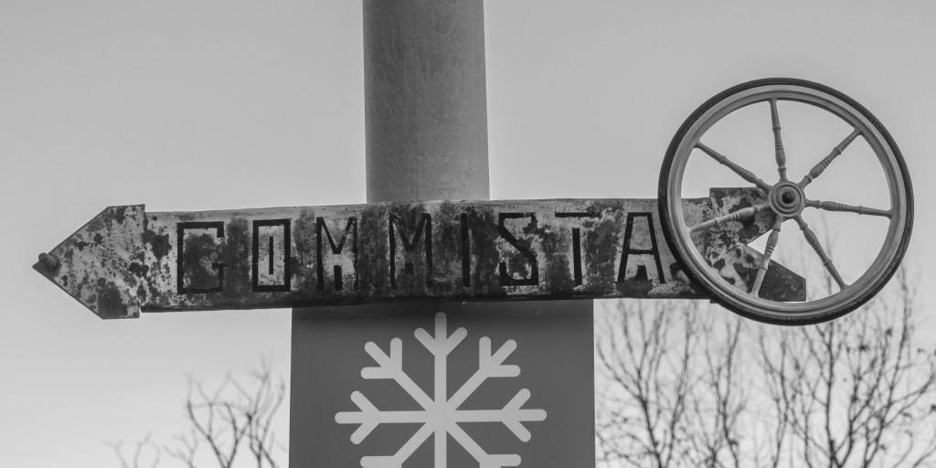 A weathered sign reading “Gommista” points left beside a wheel mounted above it.
