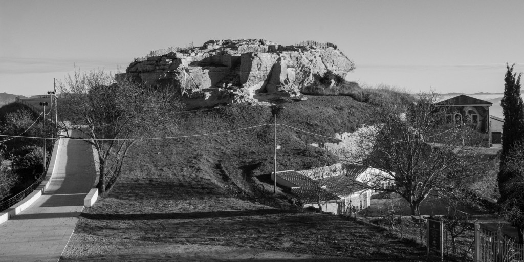 A pale rocky outcrop rises above a grassy slope, pathways and nearby buildings.