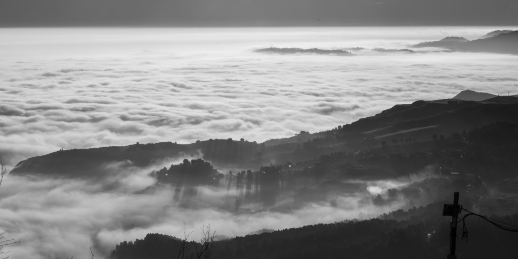 Dark hills and ridges emerge from an extensive layer of low cloud below Enna.
