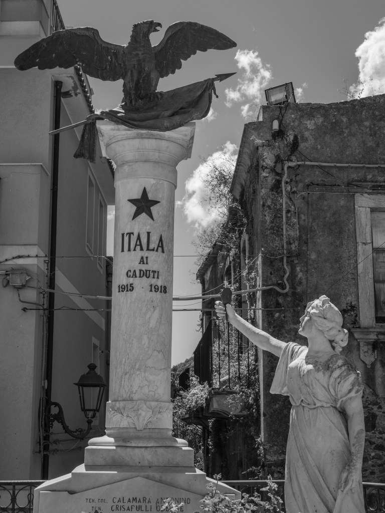 A war memorial in Itala features a tall column, an eagle and a female statue raising one arm.