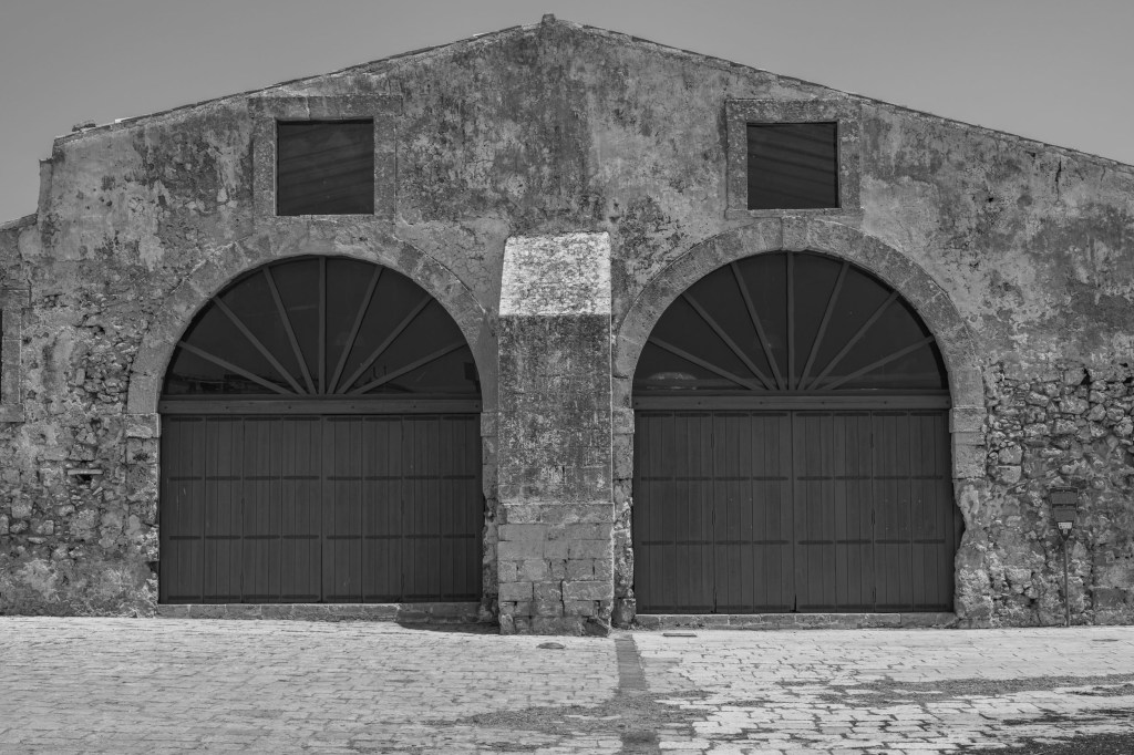 Two large arched wooden doors fill the symmetrical façade of a weathered stone building.