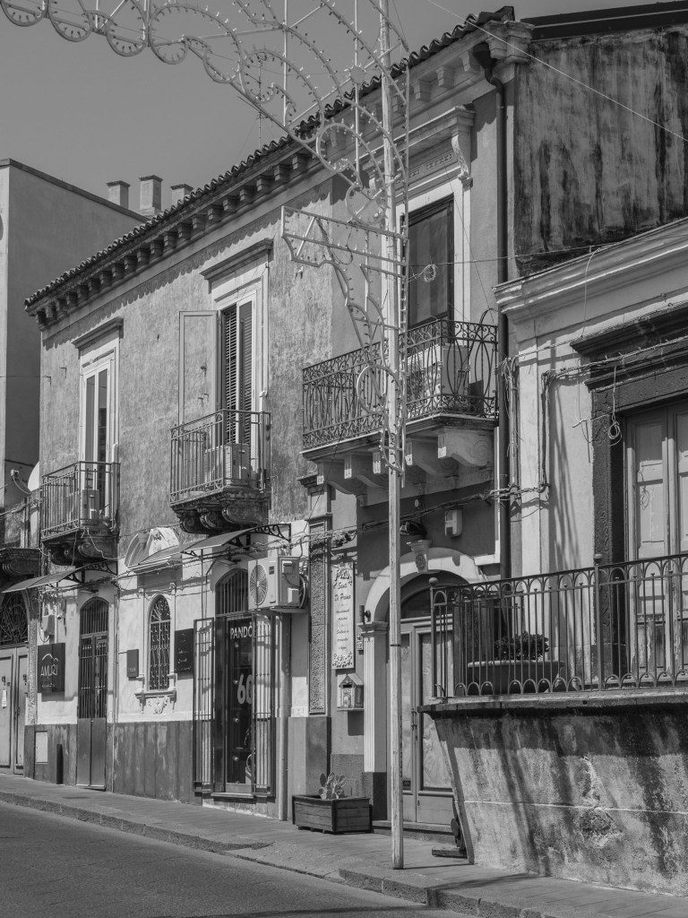 Weathered façades with balconies and shopfronts stand beneath elaborate street-festival lights.