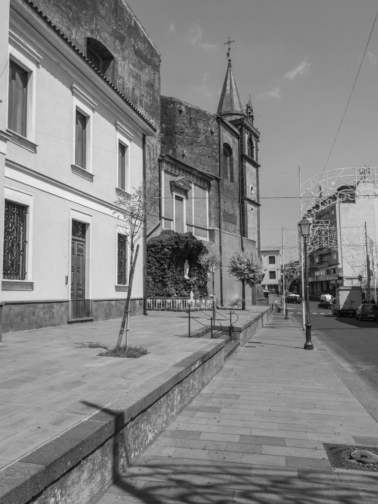 A church and bell tower rise beside a broad street decorated with festival-light structures.