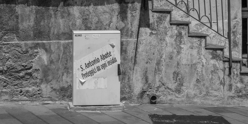 A poster asking Saint Anthony for protection from injustice is attached to a utility box beside a weathered wall and staircase.