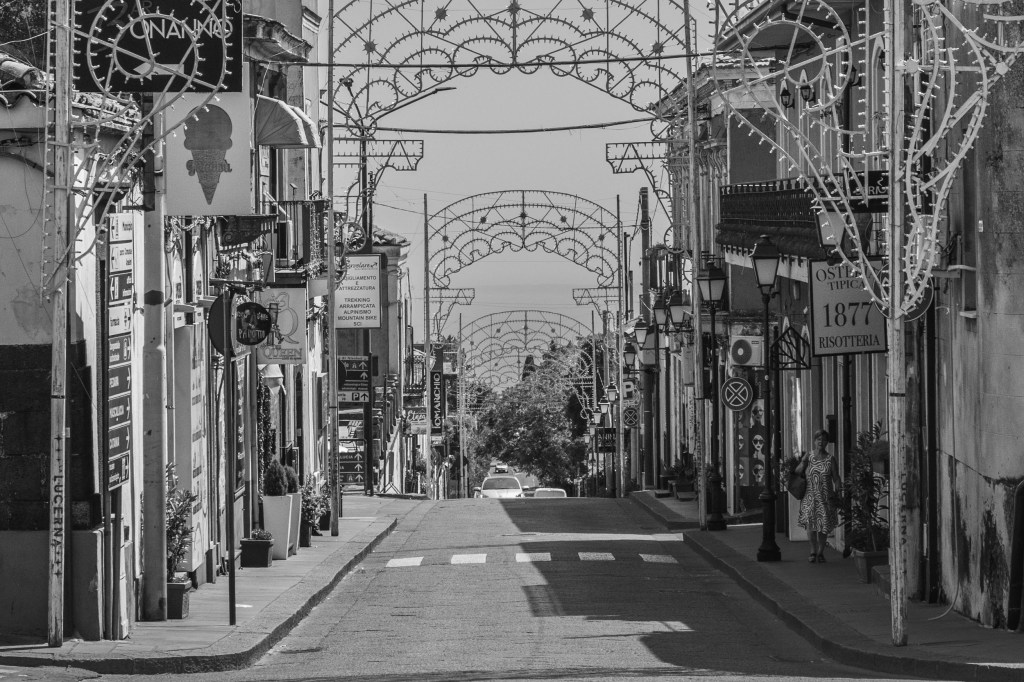 Repeated festival arches span a commercial street lined with shops, signs and a solitary pedestrian.