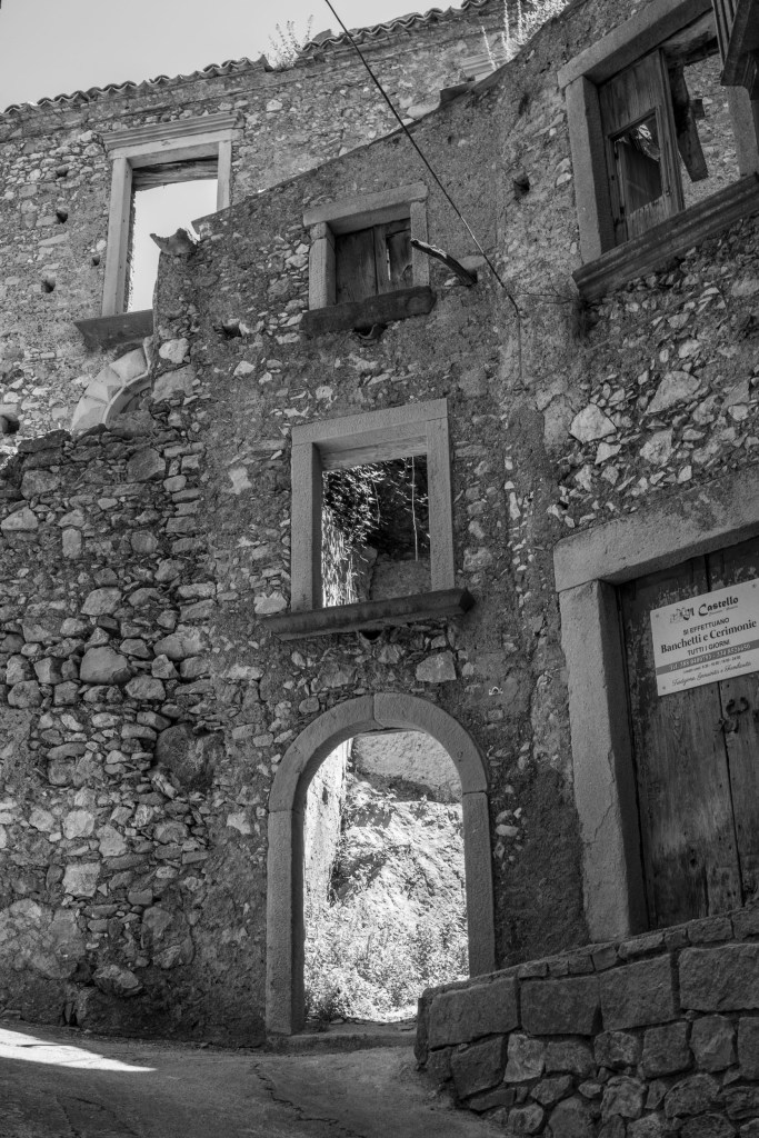 The ruined walls of a castle contain empty windows, exposed stonework and an arched passage opening onto sunlight.