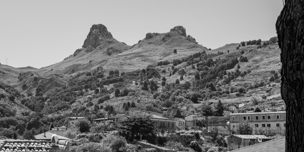 Rocky mountain peaks rise above the roofs and buildings at the edge of Novara di Sicilia.