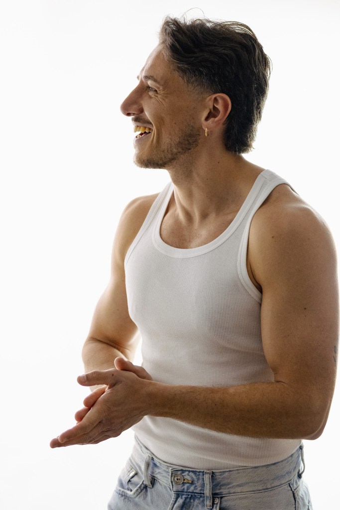 Man in profile laughing, wearing a white vest against a bright white background.