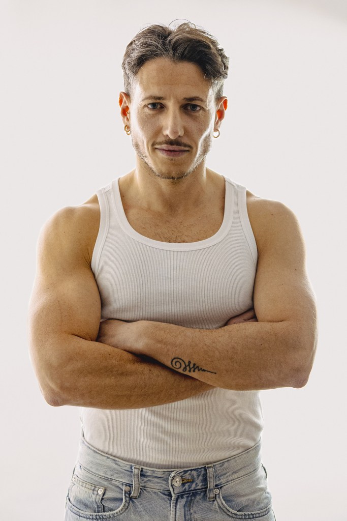 Frontal portrait of a man in a white vest with his arms crossed.