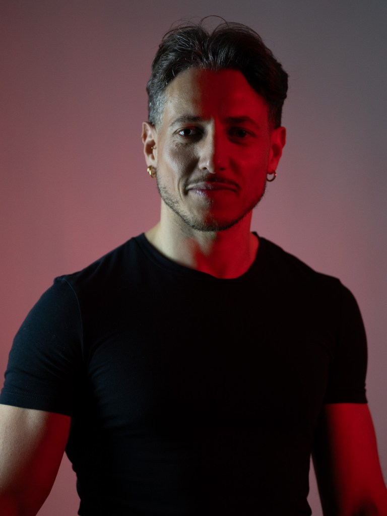 Man in a black shirt facing the camera, with red light dividing his face and body.